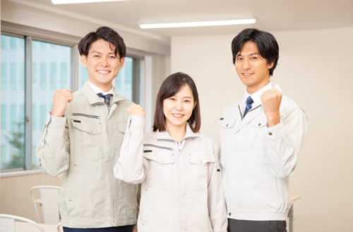 作業着を着た３人が笑顔でガッツポーズをしている様子
